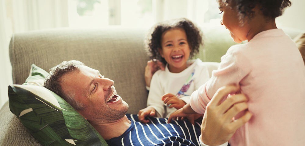 Man laughing on couch with two young girls