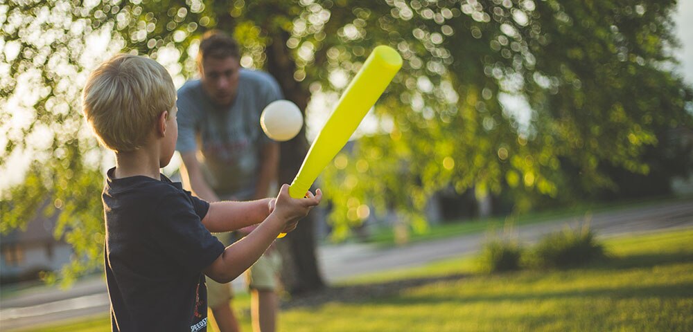 Young boy hitting a baseball to his dad