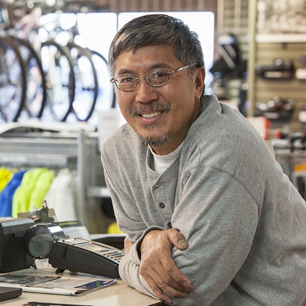 A man leaning on the sales counter of his small bicycle shop