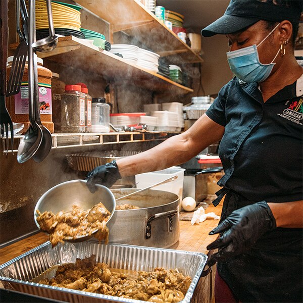 A masked kitchen worker frying fresh Jamaican food