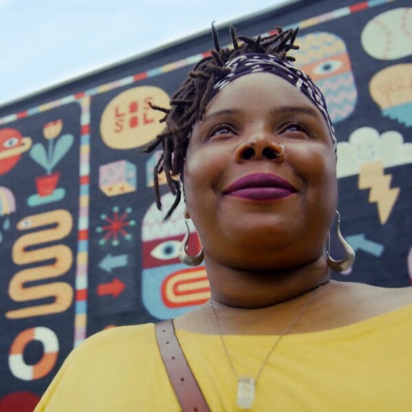 Ramat Wiley standing in front if a community mural painted on the side of a building
