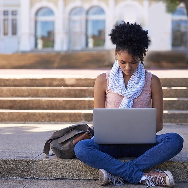 Female student sitting on college steps working on laptop