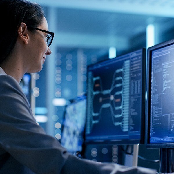 Female IT professional sitting in front of two computer monitors in a control room
