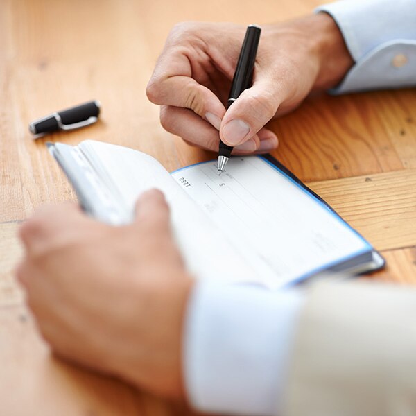 A close view of a businessman's hands as he writes a paper check out of a personal checkbook