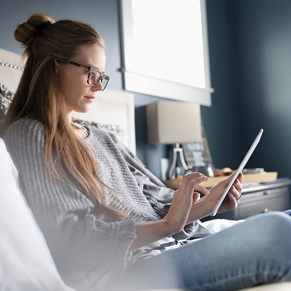 A woman with long hair sitting on a bed while using a computer tablet device