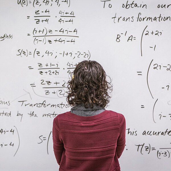 A woman with her back to the viewer looking at a whiteboard full of written complex mathematical equations