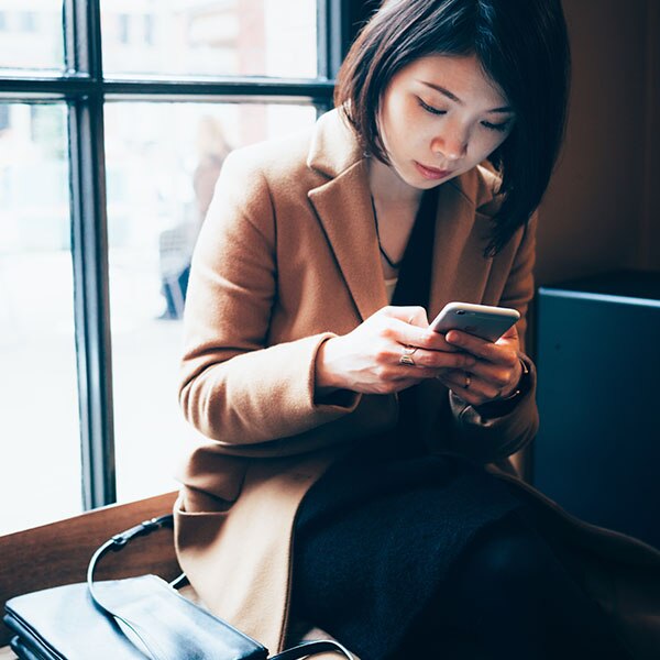 Young woman sitting in front of a window, using her cell phone