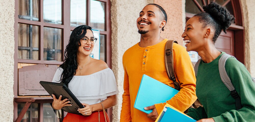 College students walking on campus holding notebooks and folders, representing funding higher education and student loan planning.