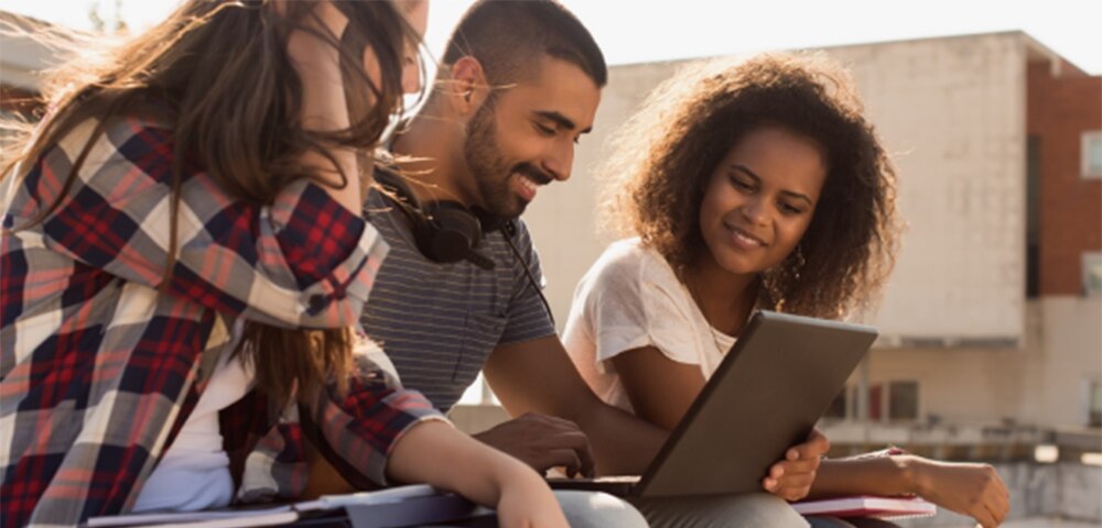Students sitting together outside, looking at a laptop.