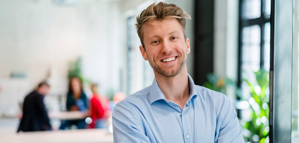 Professional standing with arms crossed in a modern office environment.