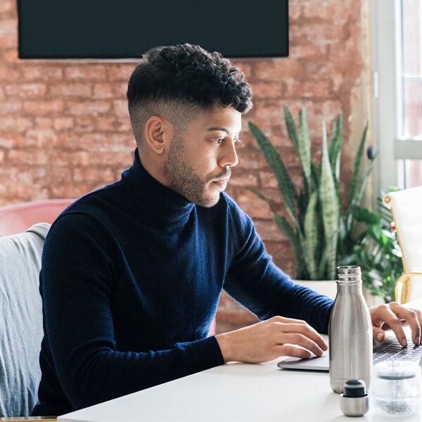 Person working at a desk with a laptop, water bottle, and notebook in a home office setting.