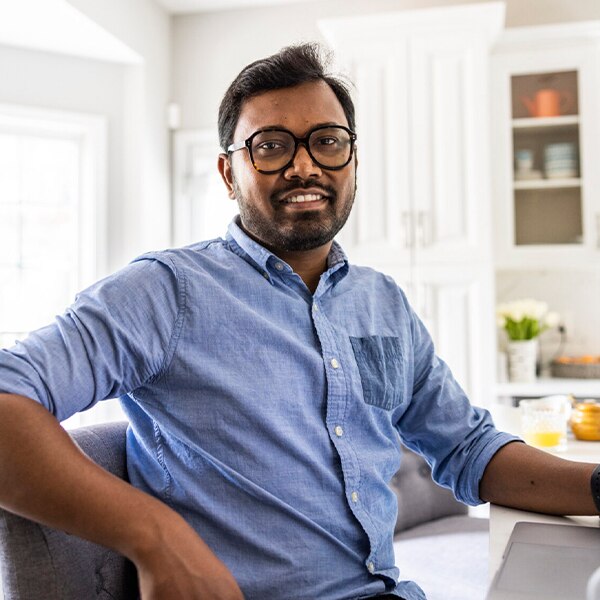 Person seated indoors in a kitchen or dining area, leaning back in a chair near a table.