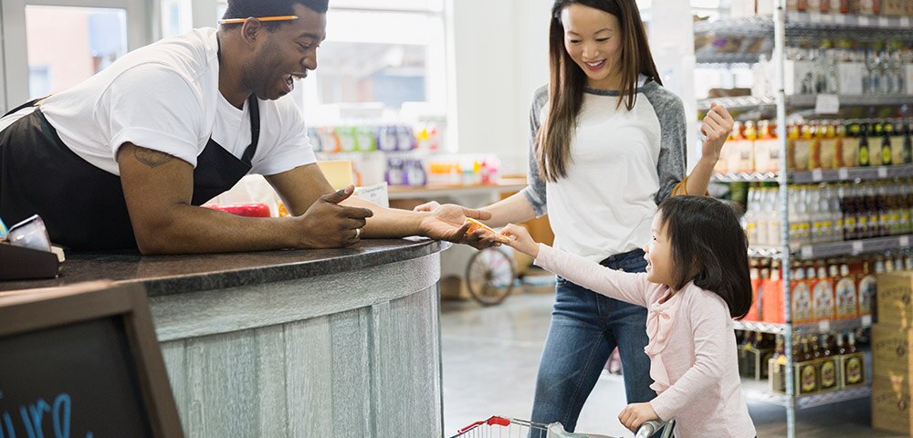 Young girl, with parent, handing something to grocery store clerk