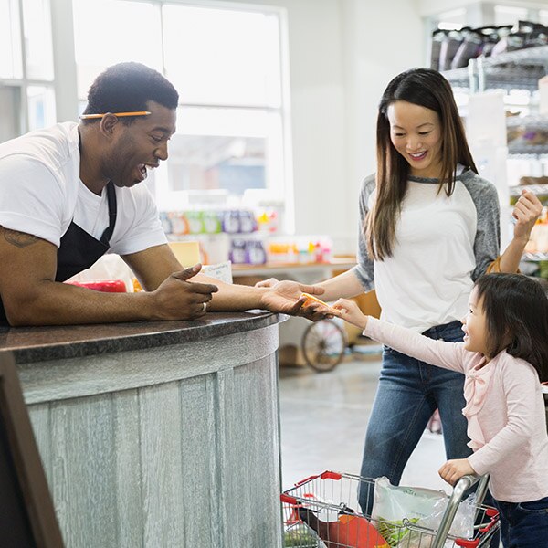 Young girl, with parent, handing something to grocery store clerk