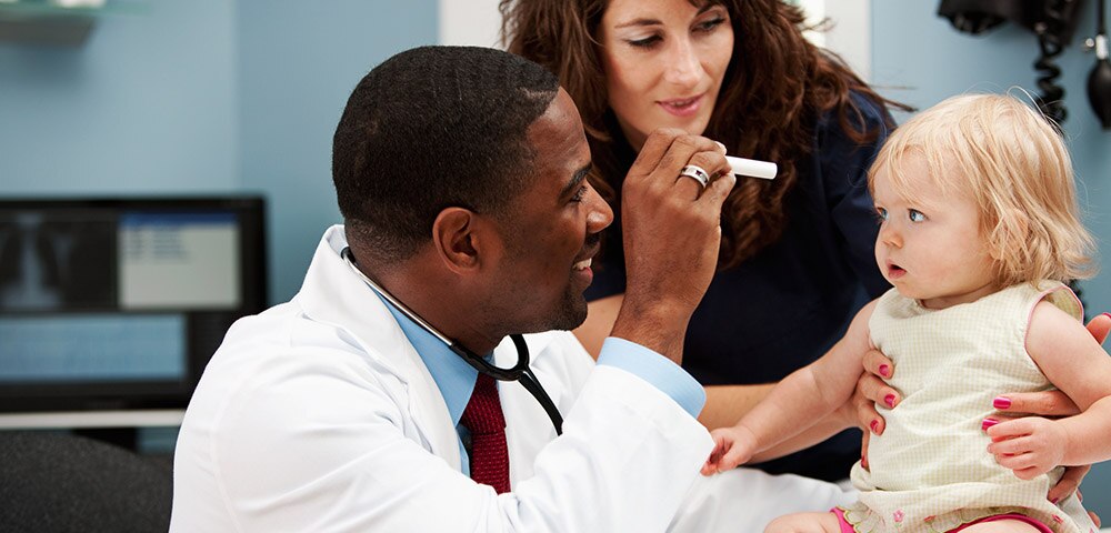 Mother holding baby girl while doctor examines her