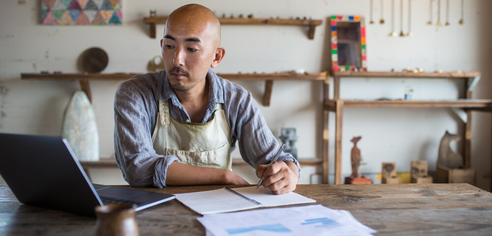 man looking at laptop and taking notes