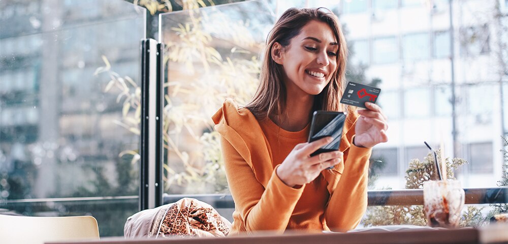 woman in orange top looking at credit card and mobile phone