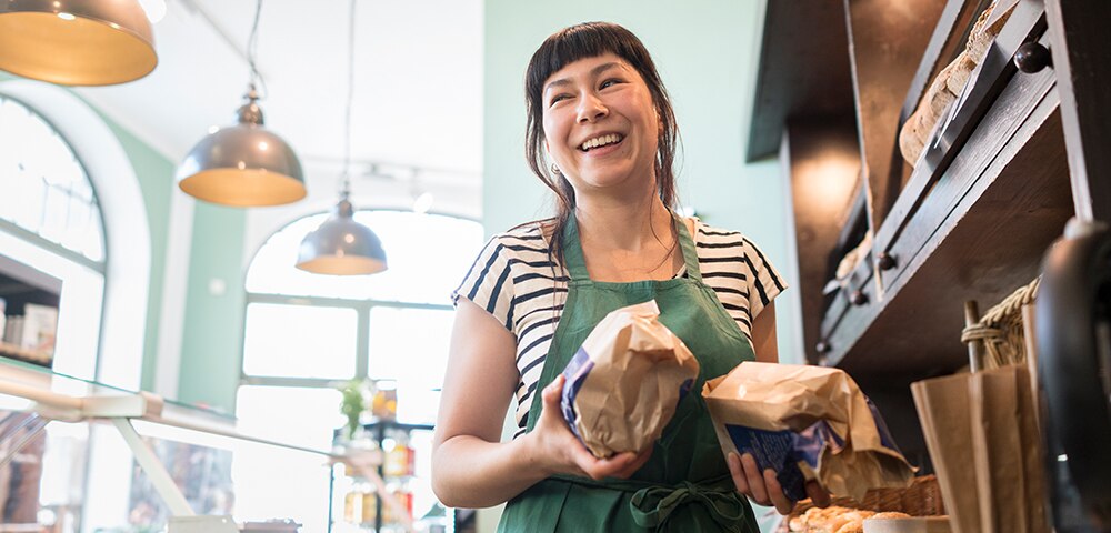woman in bakery holding loaves of bread