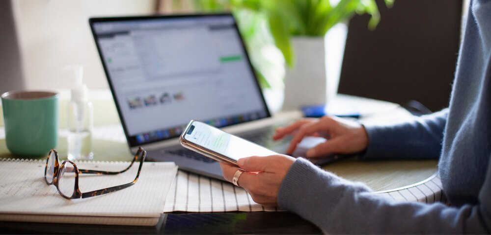 woman using laptop and holding mobile phone in hand