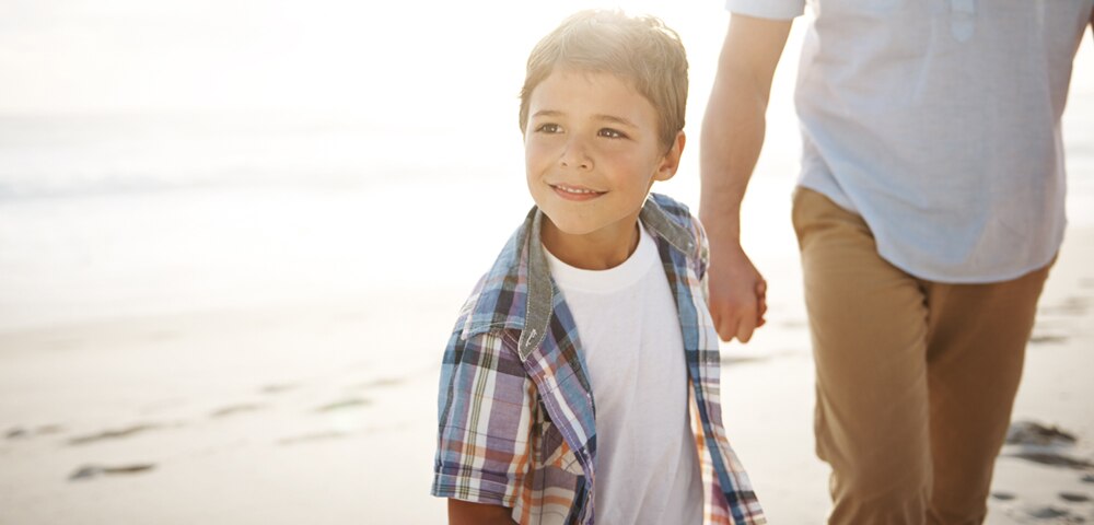 Kid holding dad's hand walking on a beach