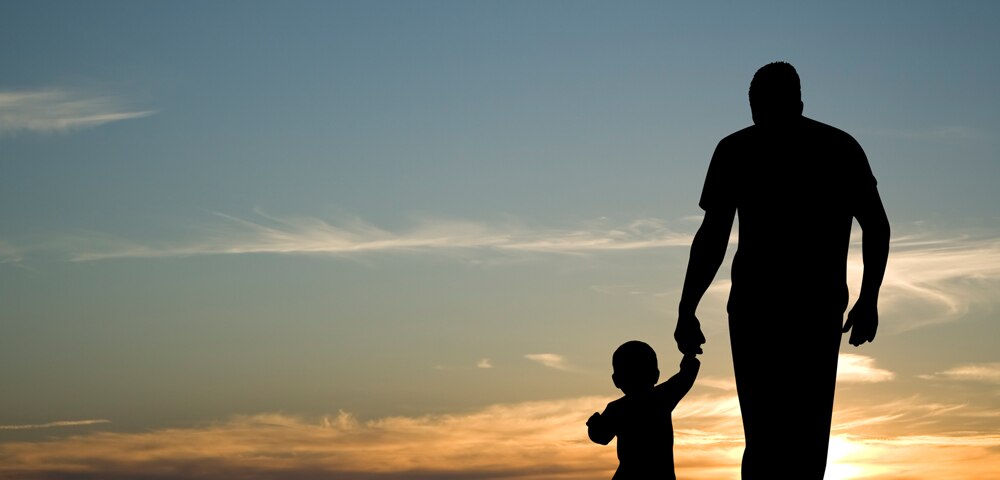 shadow outline of child holding grandfather's hand looking at the sunset sky