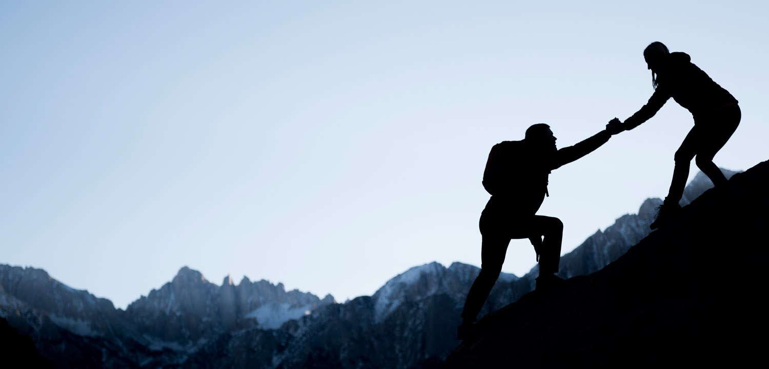 woman helping man climb a mountain