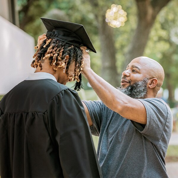 Father with heling son with graduation garments