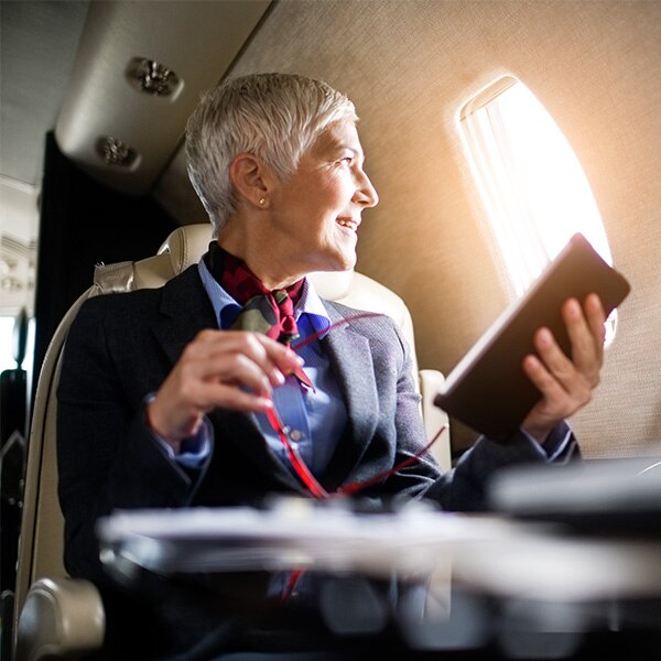 Woman looking out window of plane holding tablet.